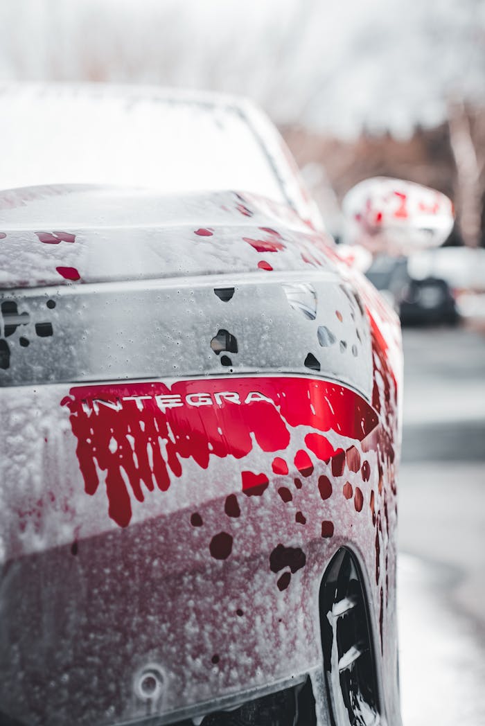 Close-up of a red Integra car being washed, showcasing water droplets and soap.